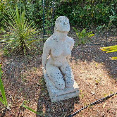 une statue représentant une femme assise sur un bloc de pierre au milieu d'un jardin