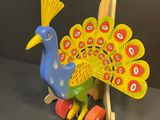 brightly colored wooden toy peacock sitting on wheels on a black background