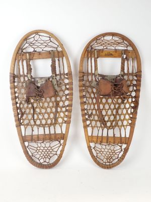 pair of old snowshoes on a white surface with a white background