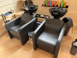 deux chaises noires dans un salon de coiffure, avec des sèche-cheveux accrochés au mur