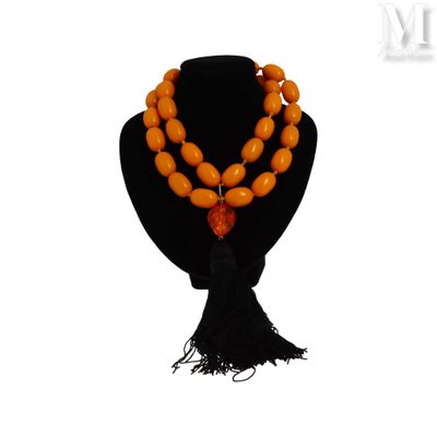 un collier de perles orange orné d'un pompon noir, posé sur un mannequin