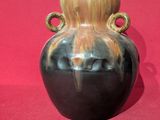a black vase with a wooden handle on a red surface