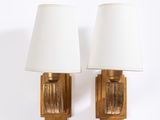 pair of brass sconces with white shades on each of them