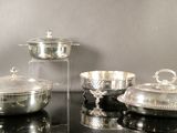 trois plats en argent posés sur une table noire recouverte d'un couvercle en verre