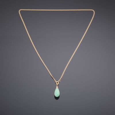 a gold necklace with a green tear shaped stone hangs from a gold chain