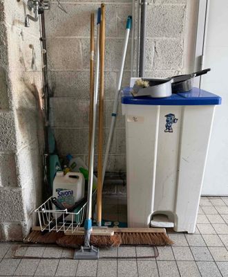 une poubelle avec des balais et une serpillière à côté d'une autre poubelle