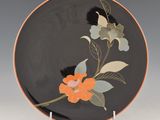 an orange and black plate with flowers and leaves on it