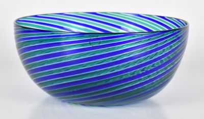 un saladier en verre rayé de bleu et de vert posé sur une surface blanche