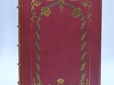 an old red book with gold trimming and a decorative frame