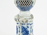 un vase bleu et blanc orné d'un couvercle doré, posé sur un socle