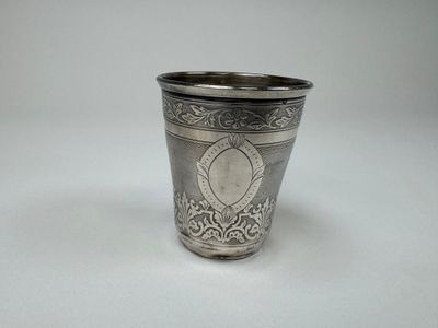 silver plated shot glass with ornate design on a plain surface