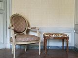 un fauteuil et un pouf dans une pièce dont l'un des murs est recouvert de papier peint