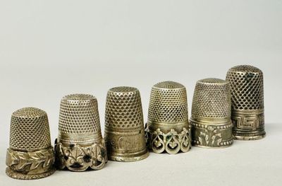 six antique thimbles lined up in a row on a white surface