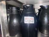 Plusieurs vases noirs sont alignés sur une étagère dans une cuisine.