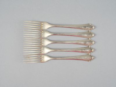 six fourchettes sont disposées en rangée sur une surface blanche