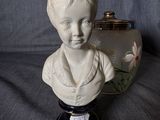 a white bust of a boy sitting on a table next to a vase