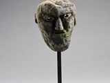 une sculpture représentant le visage d'un homme, posée sur un socle métallique