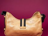 a tan leather handbag with black straps on a pink background