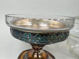 a glass bowl with a metal base on a table next to a glass vase