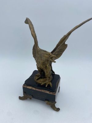 statue en bronze représentant un oiseau, posée sur un socle en marbre noir, avec un fond blanc
