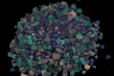 purple and green crystals are scattered on a black surface