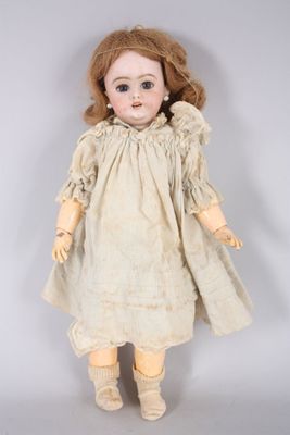 une poupée ancienne vêtue d'une robe blanche et aux cheveux bruns