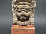 a stone head of a man with a crown on a wooden base