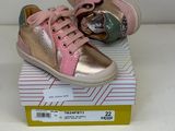 une paire de chaussons de bébé roses et dorés posés sur une boîte, sur une surface blanche
