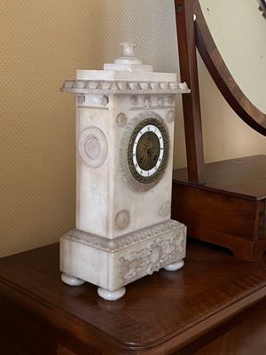 une horloge posée sur une commode, avec un miroir en arrière-plan
