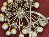 a silver brooch with pearls on it on a red cloth