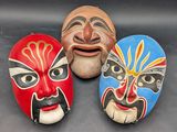 Trois masques de couleurs et de motifs différents sont posés sur une surface noire.