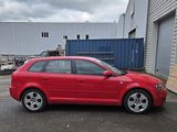 une voiture rouge garée devant un immeuble devant lequel se trouve une rampe d'accès