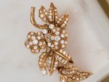 an image of a gold and diamond flower broochle on a white surface