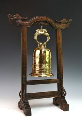 une cloche ancienne en laiton posée sur un socle en bois surmonté d'une couronne
