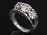 a close up of a three stone diamond ring on a black surface