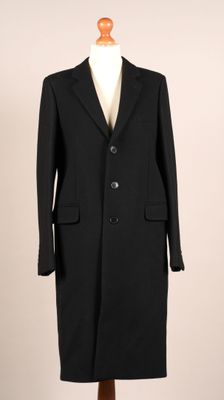 un manteau noir posé sur un pied de mannequin, avec une chemise blanche