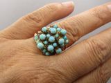 Quelqu'un tient une bague ornée d'un groupe de pierres de turquoise.
