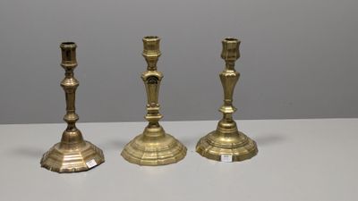 trois bougeoirs en laiton posés sur une table blanche