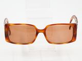 des lunettes de soleil marron posées sur un support transparent, sur une surface blanche