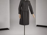 un mannequin vêtu d'un manteau et d'une jupe noirs, posé sur un socle