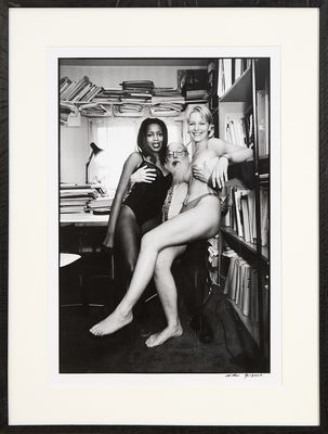 photographie en noir et blanc de deux femmes assises sur une chaise devant une bibliothèque