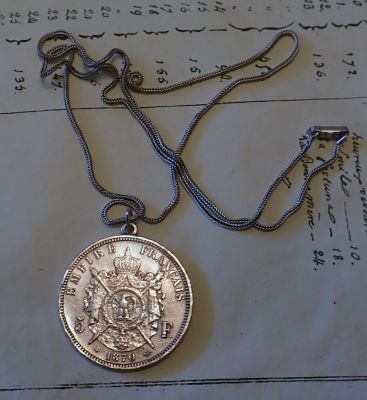 une pièce d'argent attachée à une chaîne, posée sur un morceau de papier