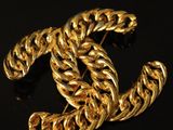 a close up of a gold chanel brooch on a black surface