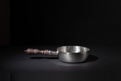 an old metal bowl with a wooden handle on a black surface