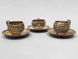 trois tasses et soucoupes en métal argenté posées sur des soucoupes, sur une table