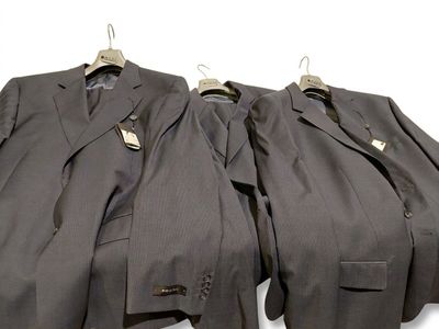 trois costumes sont suspendus à un cintre sur un fond blanc