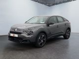 Une voiture grise est garée dans une grande pièce aux murs blancs.