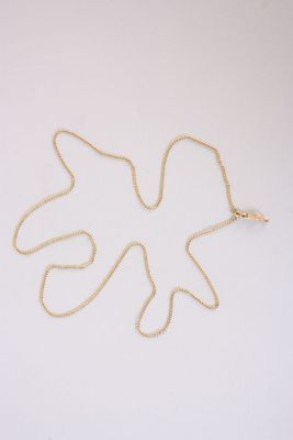 un collier en or orné d'une feuille, posé sur une surface blanche