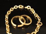 two gold wedding rings and a chain bracelet on a black surface