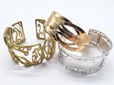 three gold and silver cuff bracelets sitting on top of each other